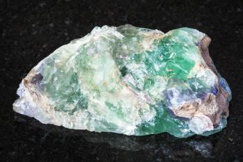 macro shooting of natural mineral - raw green Beryl, Chrysoberyl, Alexandrite gemstone on black granite from Ural Mountains