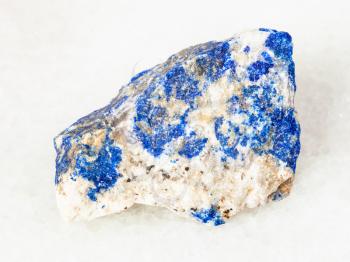 macro shooting of natural mineral - rough Lazurite (Lapis Lazuli) stone on white marble from Ural Mountains