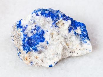 macro shooting of natural mineral - rough Lazurite (Lapis Lazuli) gemstone on white marble from Ural Mountains
