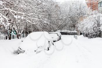 snow-covered cars on car parking along road in residential district of Moscow city in overcast winter day