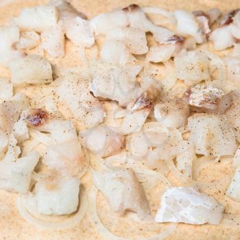 cooking of pie - stuffing from raw fish pieces and onion rings on dough