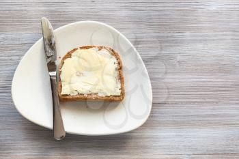 top view of bread sandwich with buttered butter and steel knife on white plate on gray wooden board with blank copyspace