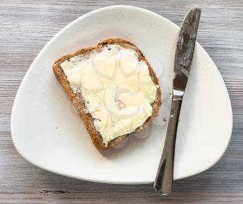 top view of bread sandwich with buttered butter and steel knife on white plate on gray table