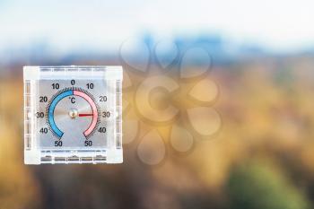 view of outdoor thermometer on home window and blurred urban park in hot autumn day