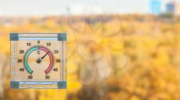 outdoor thermometer on home window and blurred yellow urban garden on background in sunny warm autumn day