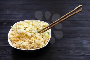Chinese cuisine dish - bowl with Fried Rice with Shrimps, Vegetables and Eggs (Yangzhou rice) with chopsticks on dark wooden table
