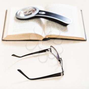 reading book with low vision - spectacles and loupe on open book on pale table (focus in the foreground)