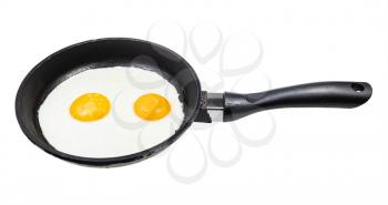 two fried eggs in black frying pan isolated on white background