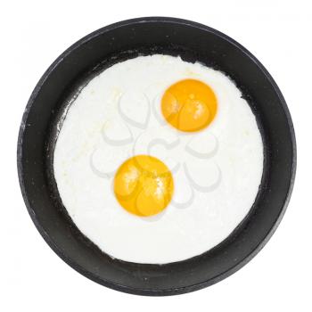top view of two fried eggs in black round pan isolated on white background