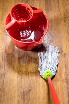 point of view of rope mop cleans wooden laminate floor near bucket with water at home