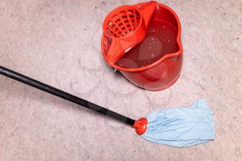 mop washes linoleum floor near red bucket with water at home