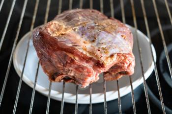 cooking Roast beef at home - piece of beef coated with marinade and spices on grill grate at home kitchen