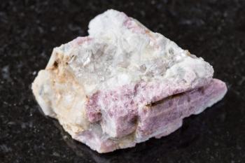 macro photography of sample of natural mineral from geological collection - unpolished pink Tourmaline mineral in feldspar and quartz rock from Kalba Range, Kazakhstan on black granite background