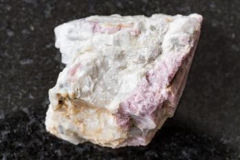 macro photography of sample of natural mineral from geological collection - raw pink Tourmaline mineral in feldspar and quartz rock from Kalba Range, Kazakhstan on black granite background