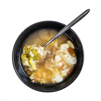top view of soup with stelline (italian pasta) and vegetables (cauliflower, broccoli, etc) in black bowl with spoon isolated on white background