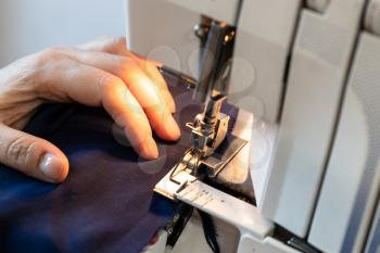 seamstress processes the edge of fabric on serger close up at home