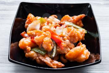 korean cuisine - portion of stir-fried Shrimps with cashew nuts and vegetables in sweet and sour sauce (Shrimps Combo) in black bowl close up