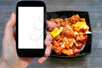 travel concept - tourist photographs of Chinese cuisine dish Pork in sweet and sour sauce on smartphone with empty cutout screen with blank place for advertising
