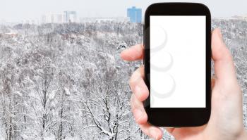 travel concept - tourist photographs of snowy city park and residential district in winter in Moscow city on smartphone with empty cutout screen with blank place for advertising