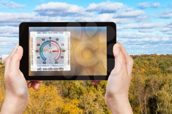 travel concept - tourist photographs city park and outdoor thermometer on home window in hot autumn day on smartphone in Moscow, Russia