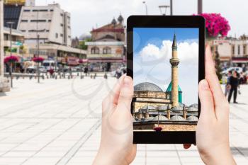 travel concept - tourist photographs of Mausoleum of Jalal ad-Din Muhammad Rumi (Mevlana) and Dervish Lodge (Tekke) on Muze Alani square in Konya city on smartphone in Turkey in spring