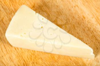 top view of piece of local italian Pecorino Romano sheep's milk cheese on light wooden cutting board
