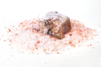raw Halite mineral in pile of grained pink Himalayan Salt on white background