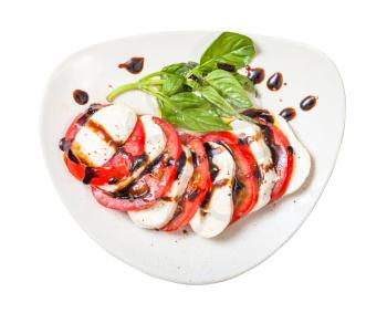 italian cuisine insalata caprese (caprese salad) - top view of sliced mozzarella cheese and tomato with basil twig seasoned by olive oil and balsamic vinegar on plate isolated on white background