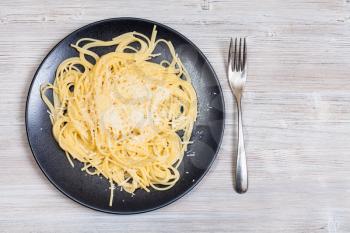 italian cuisine - top view of spaghetti al burro e parmigiano (pasta with butter and cheese) on black plate and fork on gray wooden background with blank copyspace