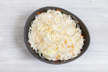 top view of Russian sauerkraut (sour cabbage pickled with carrots and served as salad) in black bowl on gray wooden background