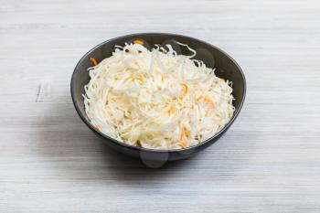 Russian sauerkraut (sour cabbage pickled with carrots and served as salad) in black bowl on gray wooden table
