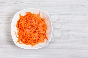 top view of Korean-style carrots ( Koryo-saram, spicy pickled carrot) in bowl on gray wooden background with copyspace
