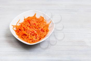 Korean-style carrots ( Koryo-saram, spicy pickled carrot) in bowl on gray wooden table with copyspace