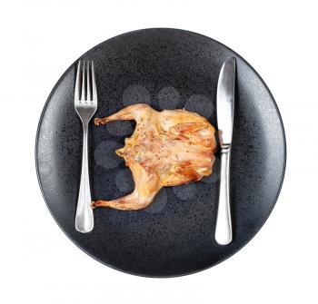 top view of roasted whole flattened quail with fork and knife on black plate isolated on white background