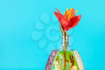 handmade artificial paper red flower in handpainted glass brandy bottle on aquamarine pastel color background