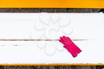 forgotten red female glove on yellow wooden bench covered by snow in winter