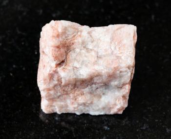 closeup of sample of natural mineral from geological collection - unpolished Feldspar rock on black granite background