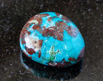 closeup of sample of natural mineral from geological collection - tumbled Chrysocolla with Cuprite rock on black granite background