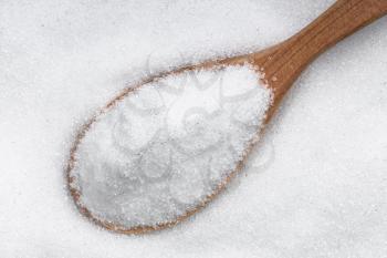 top view of wood spoon with crystalline erythritol sugar substitute close up on pile of sugar