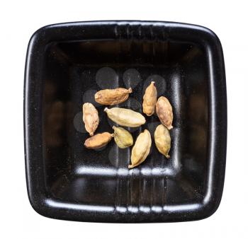 top view of several cardamom pods in black bowl isolated on white background