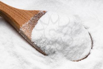 above view of wooden spoon with dextrose sugar close up on pile of sugar