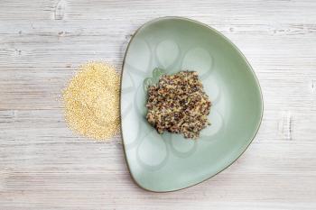 top view of quinoa grains and boiled porridge on green plate on wooden table