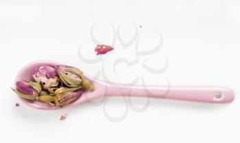 top view of old dried rosebuds in ceramic spoon on white plate