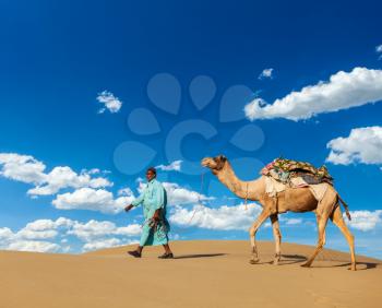 Rajasthan travel background - Indian cameleer (camel driver) with camels in dunes of Thar desert. Jaisalmer, Rajasthan, India