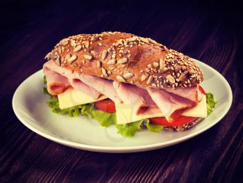 Vintage retro effect filtered hipster style image of ham sandwich with lettuce, cheese, tomato on plate on wooden table