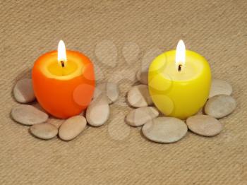 Two multicolored glowing candles on a woolen fabric background.
