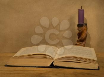 Old open book and  candle on a wooden table.