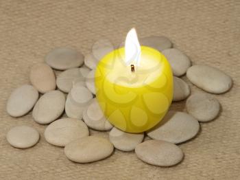 Yellow candle and small stones on a woolen fabric background.