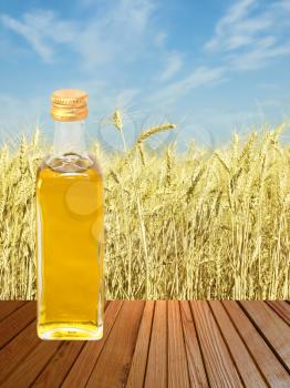 Vegetable oil on wooden surface against of yellow wheat ears and blue sky.