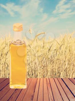 Vegetable oil on wooden table against of wheat ears and sky background.Toned image.